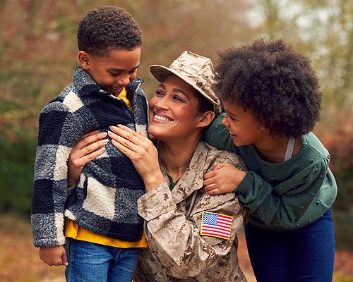 A service member embracing her two children outdoors